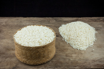 Rice in a wicker rice and scattered near on dark wooden table