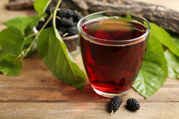 Glass of refreshing mulberry juice with berries on table close up