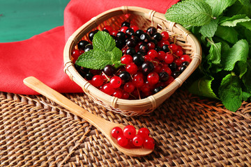Ripe red and black currant in wicker basket on wooden background