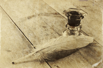 photo of white Feather and inkwell on old wooden table
