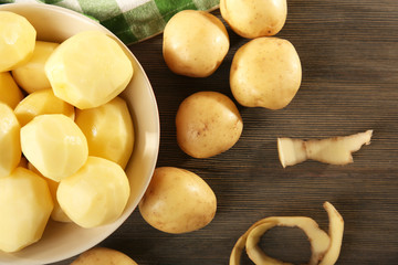 Peeled new potatoes in bowl on wooden table with napkin, top view