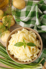 Mashed potatoes in bowl on wooden table with checkered napkin, top view