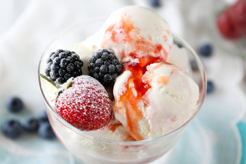 Delicious ice cream with fresh frozen berries and sauce, on color wooden background