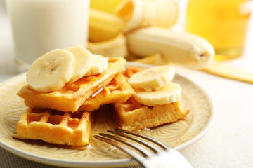 Sweet homemade waffles with sliced banana on plate, on light background
