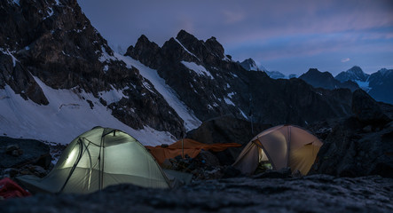 Mountaineers camps in very high craggy mountains beside glacier.