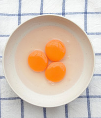 Three yellow egg yolks in white bowl (top view)