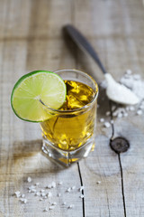 Tequila shot with lime and sea salt on rustic wooden board, selective focus