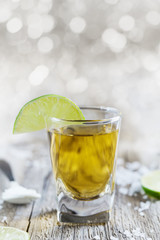 Tequila shot with lime and sea salt on rustic wooden board, selective focus