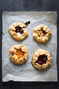 Homemade pies with plums, apricots, sour cherries and peaches on the baking paper on chalkboard background
