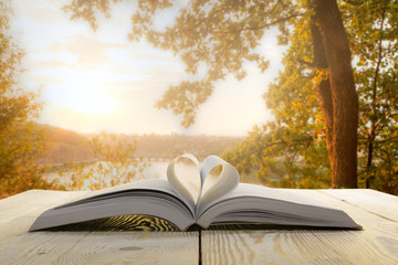 Obraz premium Open book on wooden table on natural blurred background. Heart book page. Back to school. Copy Space