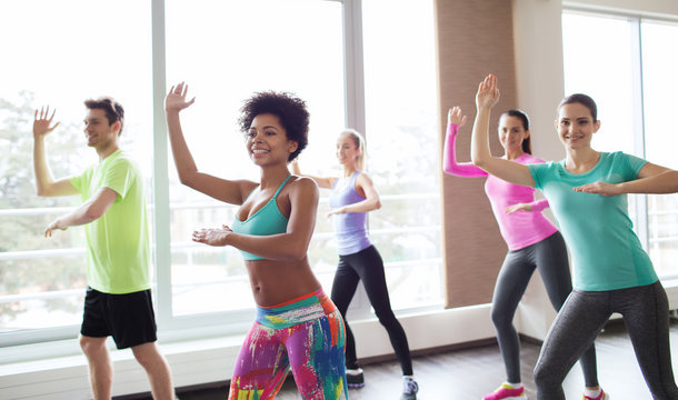 group of smiling people dancing in gym or studio