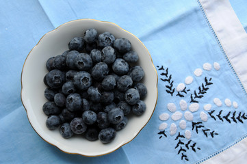 American blueberries (vaccinium corymbosum in small bowl on blue tablecloth with homemade embroidery