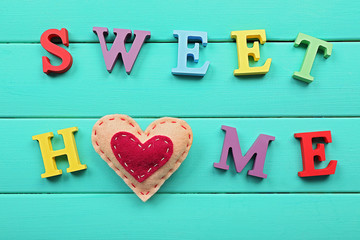Decorative letters forming words SWEET HOME with heart on wooden background