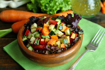 Wooden bowl of fresh vegetable salad on napkin, closeup