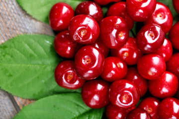Sweet cherries with green leaves on wooden background