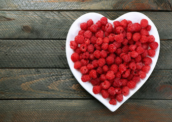 Sweet raspberries on plate, on wooden  background