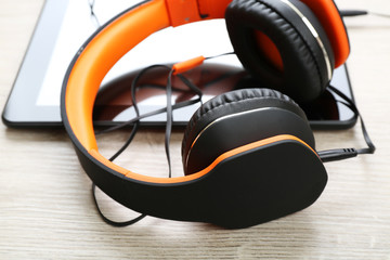 Headphones with tablet on wooden table close up