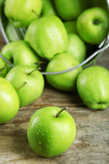 Ripe green apple in metal bucket on wooden table close up