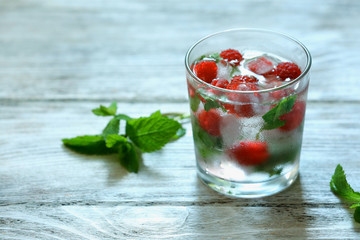 Glass of cold refreshing summer drink with berries and ice cubes on table close up