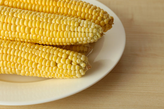 Fresh corn on cobs in plate on wooden table, closeup