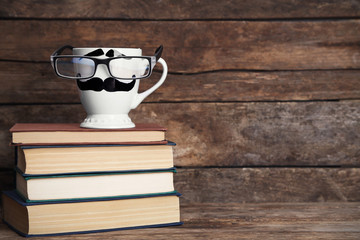 Vintage books and cup with mustache on wooden background