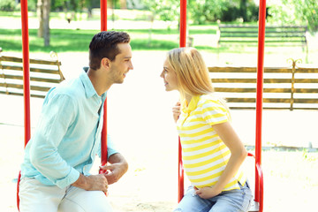 Obraz premium Young pregnant woman with husband on swing outdoors