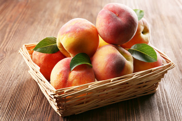 Fresh peaches in wicker basket on wooden table, closeup