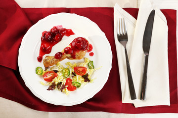 Dish of baked chicken leg and vegetable salad in white plate on table with napkin, top view