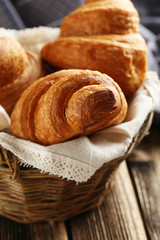 Tasty croissants in basket on brown wooden background