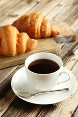 Tasty croissants with cup of coffee on brown wooden background