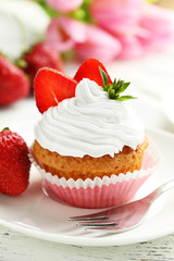 Tasty cupcake with fresh strawberry on white wooden background