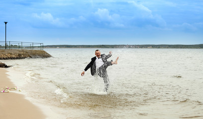 Mężczyzna chlapie wodą na brzegu jeziora. - obrazy, fototapety, plakaty