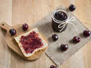 Cherry jam and toast on wooden background