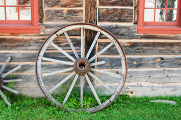 Fototapeta na wymiar old wagon wheel standing against a log cabin wall