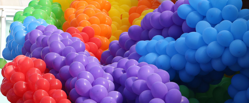 Groups of violet, blue, red, orange, yellow, green balloons together making cheerful colorful pile