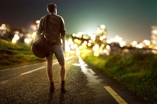 Guy walks towards city lights on a country road
