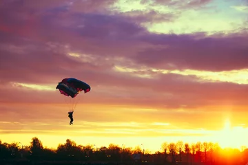 Tuinposter Luchtsport Skydiver op kleurrijke parachute in zonnige lucht