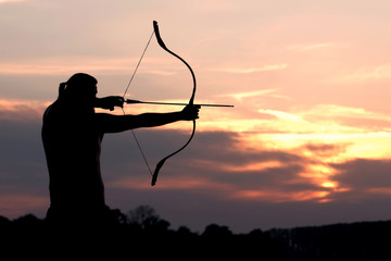 Silhouette archery shoots a bow at a target in sunset sky