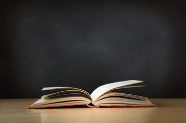 Old Book Opened on Desk with Chalkboard in Background