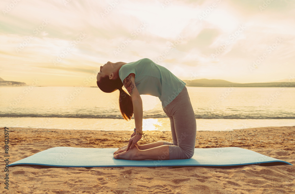 Wall mural Girl doing yoga exercise on beach at sunset