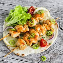 chicken kebabs and fresh vegetable salad on a homemade tortilla on a light wooden background