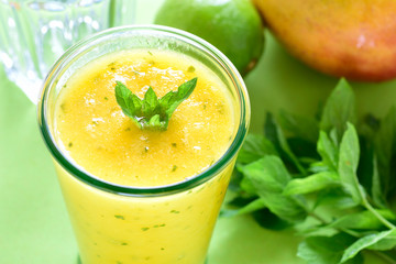 Cooling Mango mint smoothie, summer drink on green table, Yellow Tropical Smoothie made with mango, mint and lime juice.