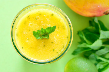 Cooling Mango mint smoothie, summer drink on green table, Yellow Tropical Smoothie made with mango, mint and lime juice.