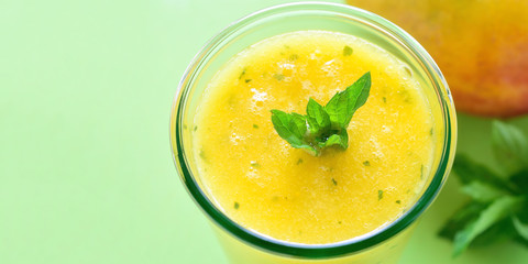 Cooling Mango mint smoothie, summer drink on green table, Yellow Tropical Smoothie made with mango, mint and lime juice. Copy space.