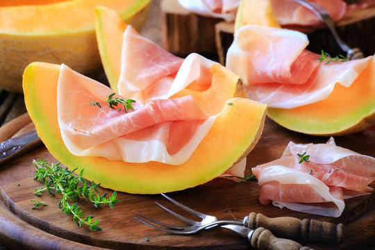Italian prosciutto with melon with fresh thyme on rustic wooden kitchen table