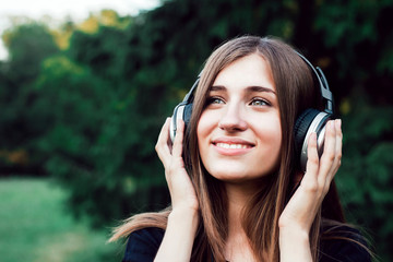 Beautiful young girl listening to music on headphones. The girl in the park .