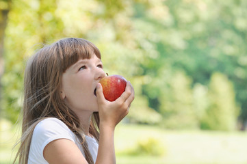 happy girl eating apple on picnic in the park in sunny summer day