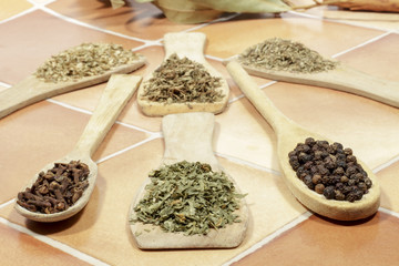 Dried parsley beside black pepper and cloves, with other spices behind