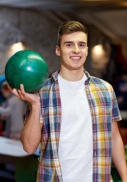 happy young man holding ball in bowling club