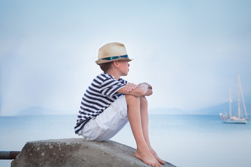 Thoughtful boy looks at ship at sea and dreams